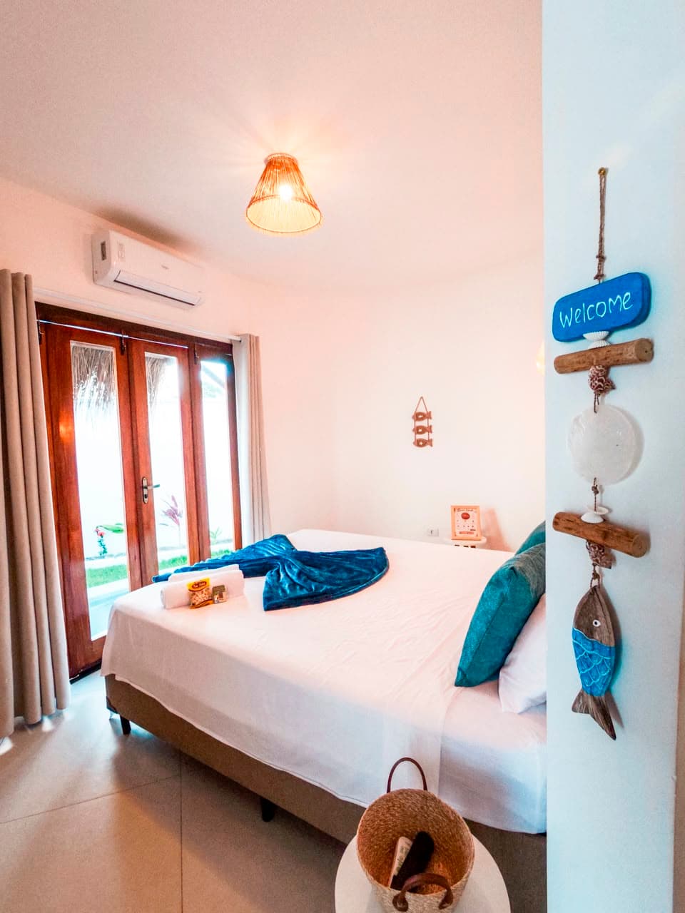 Quarto do bangalô aconchegante com cama queen, detalhes em azul e enfeite Welcome na parede